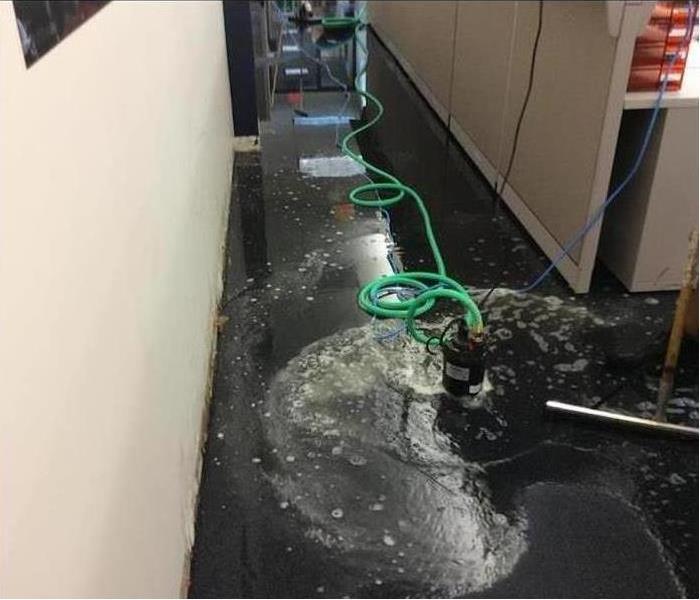 hallway with dark blue carpet covered in water with a pump extracting the water