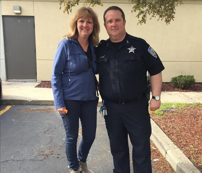 female employee standing with a police officer in front of a tan building