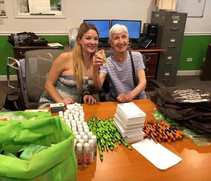 two employees sitting behind a table with SERVPRO promotional items