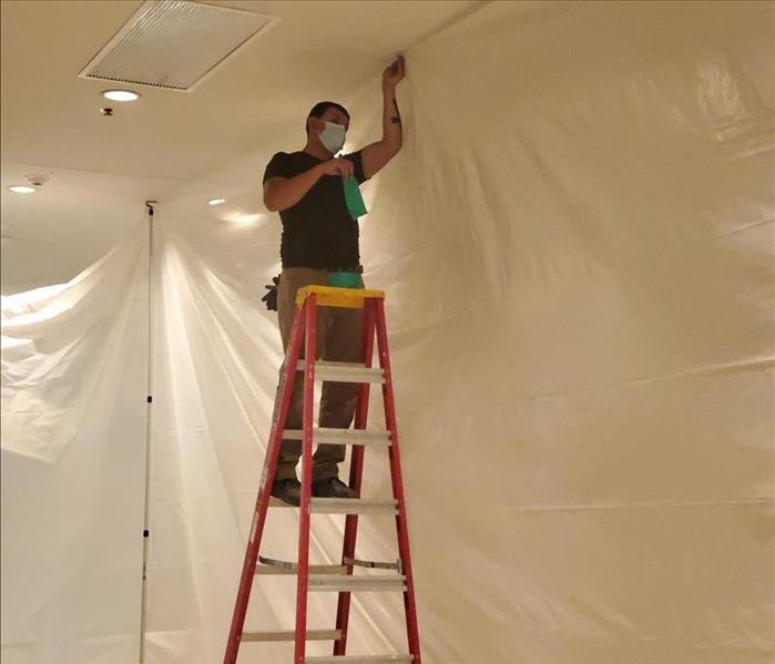 SERVPRO technician on a ladder by plastic-covered wall