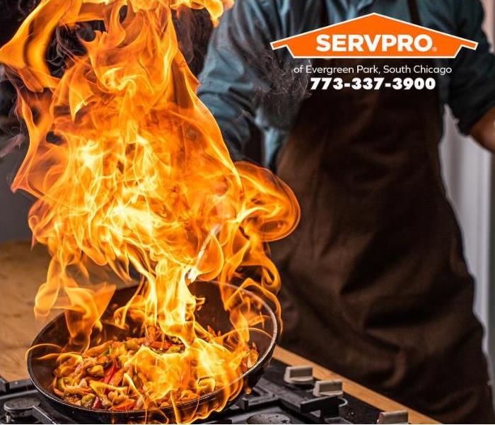 Flames erupt from a pan while a chef cooks in a hotel kitchen.