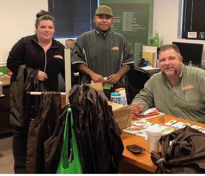 Three SERVPRO employees in a room smiling at the camera. 