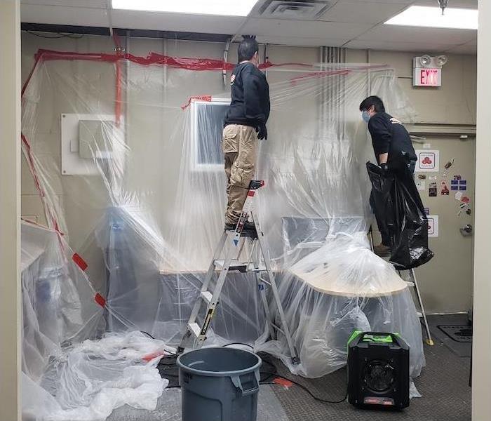 Two SERVPRO technicians installing plastic to protect contents from water damage in an office